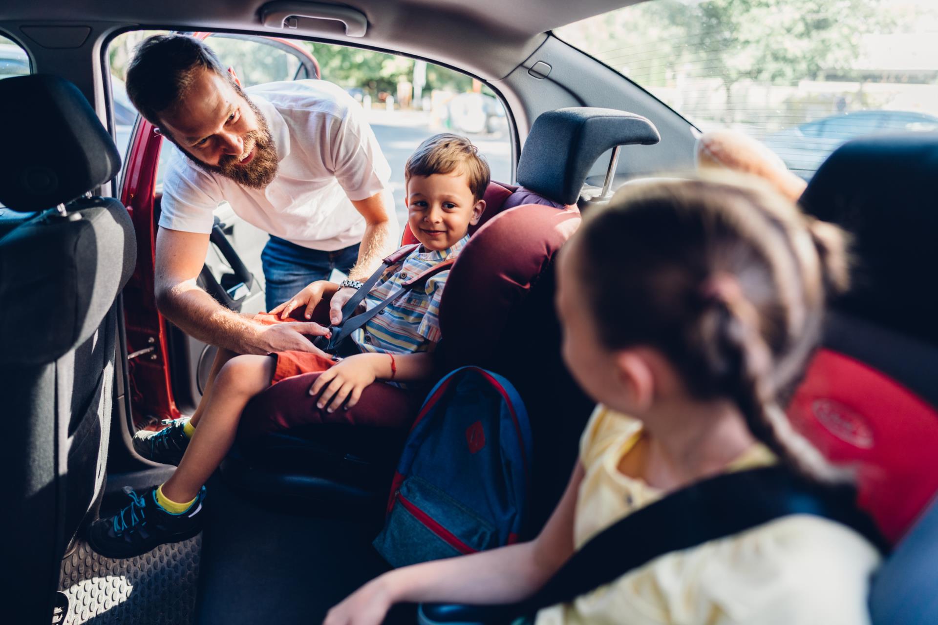 Caregiver helping child get buckled into their car seat.